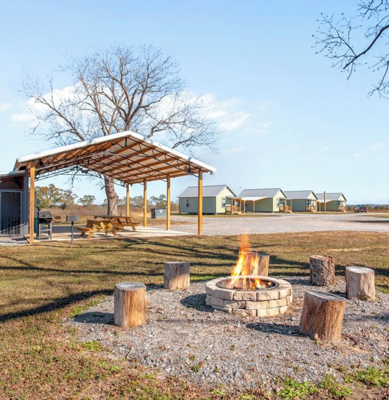 Covered pavilion with grills and picnic tables beside a stone fire pit